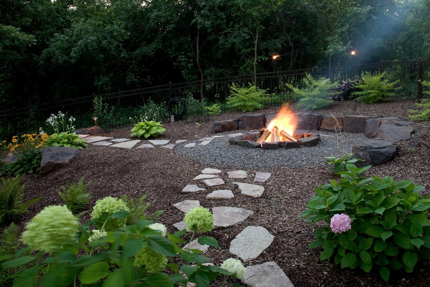 Flagstone paver walkways leading to an in-ground fire pit surrounded by crushed gravel.
