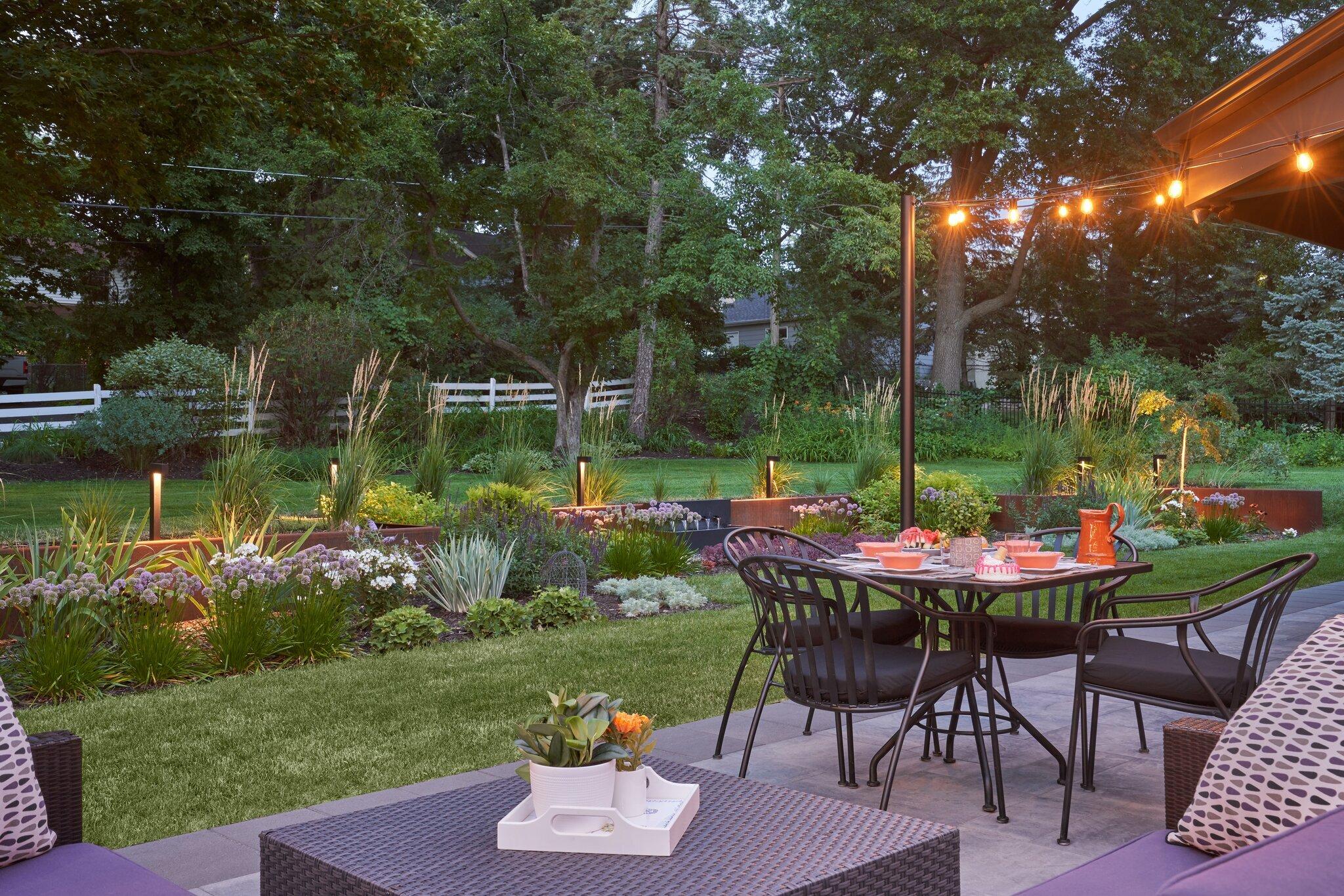 grey belgard modern patio with bistro lights overlooking colorful garden bed with modern lighting and corten steel