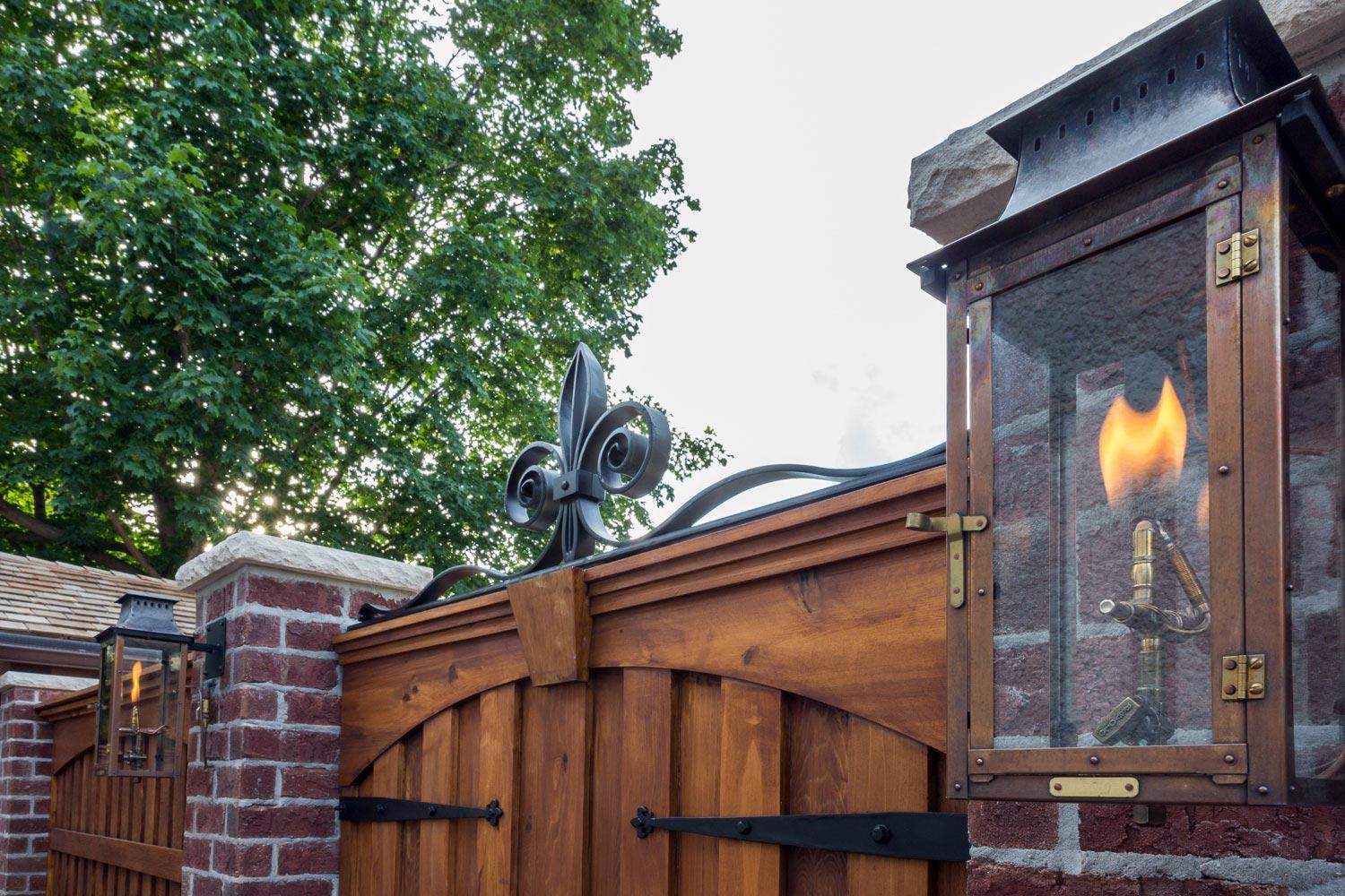 Gas lamps and a iron fleur-de-lis accent this brick courtyard gate.