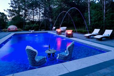 Two chairs in the swimming pool with illuminated water feature bowls and laminar jets ino the surface of the pool.