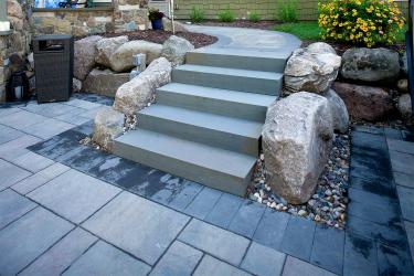 Outdoor stone stair case, boulder retaining wall, and paver patio.