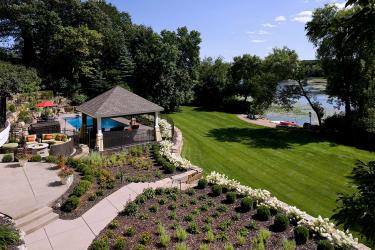 Terrance backyard patios with gazebo, pool, and matrix of perennial plantings, overlooking a green lawn, beach and lake.