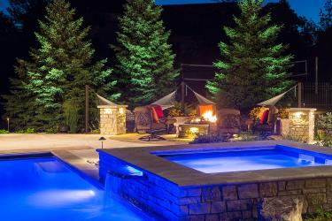 backyard hot tub and swimming pool with dramatic blue lighting