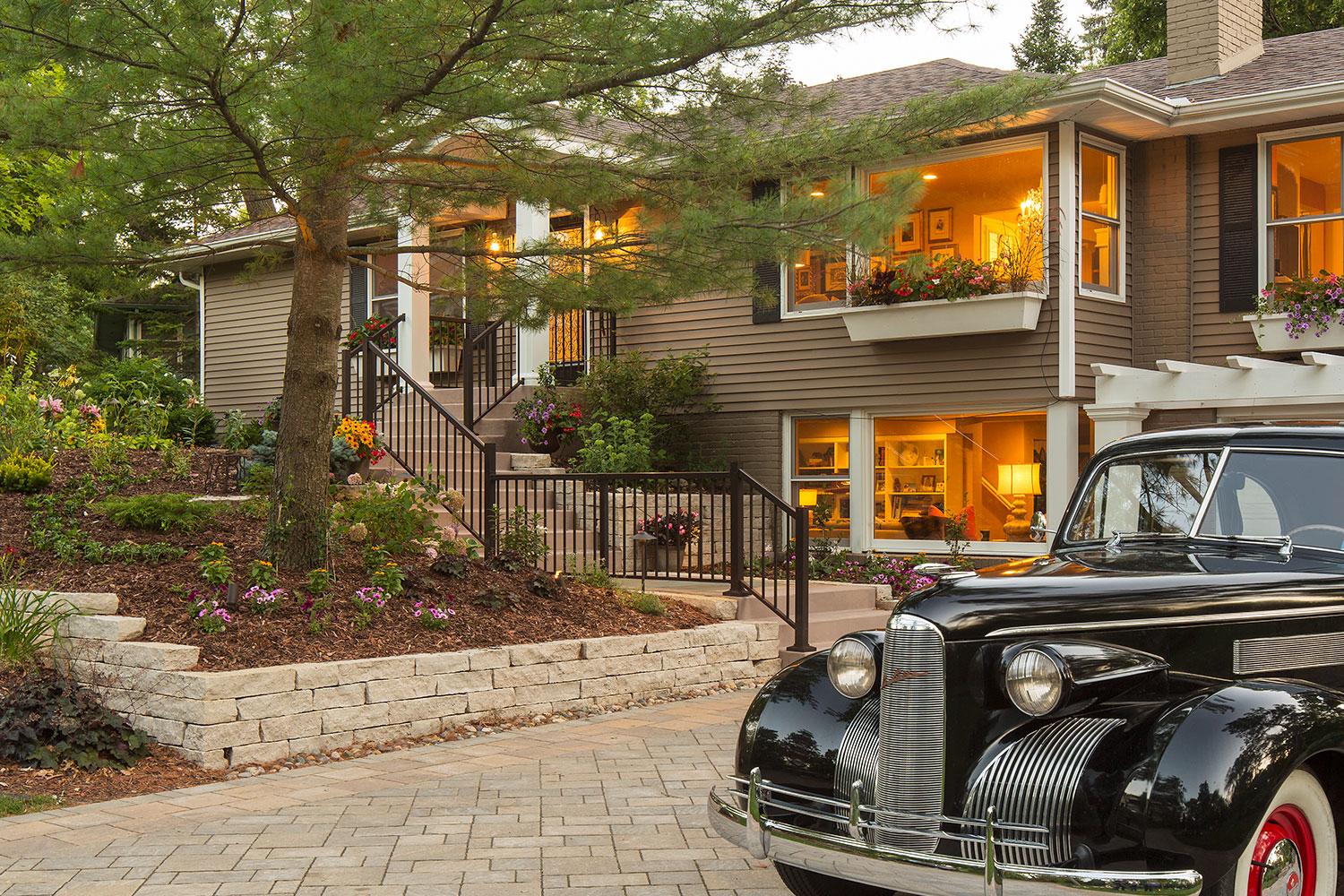 Paver driveway, limestone retaining wall, plantings, and a classic car.