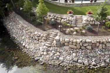 Tiered boulder wall created with tons of rock, black fence and plantings