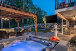 Hot tub with laminar jet overlooking a paver patio with cedar pergola and a backyard kitchen