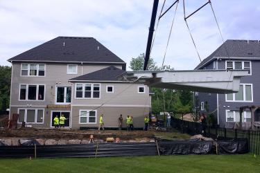 Construction crane installing a preformed fiberglass swimming pool in the ground.