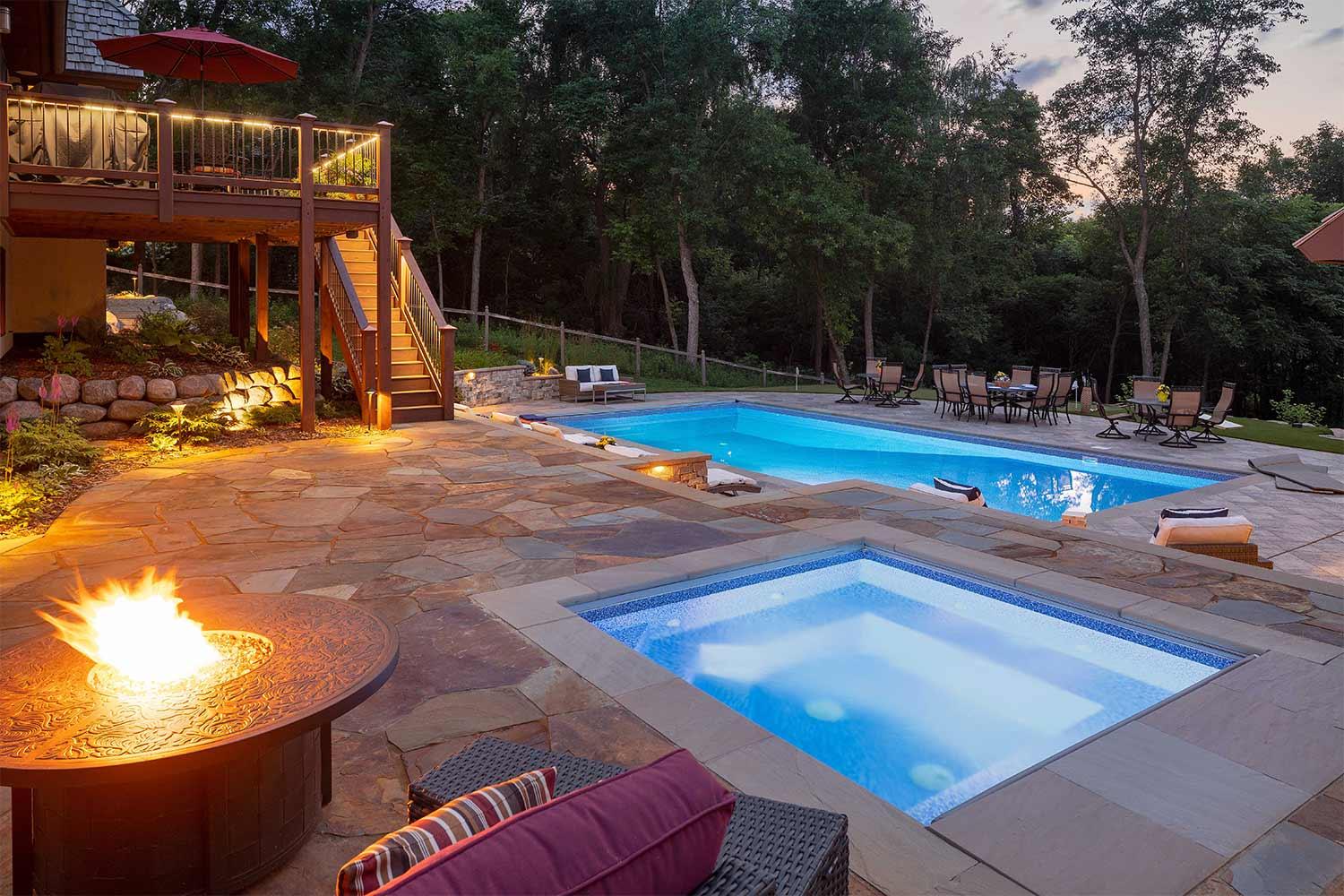 Fire table, hot tub, and swimming pool at dusk.