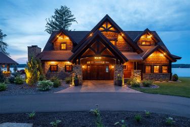 Lake shore chalet-style home with a circle drivewal and warm night lighting.