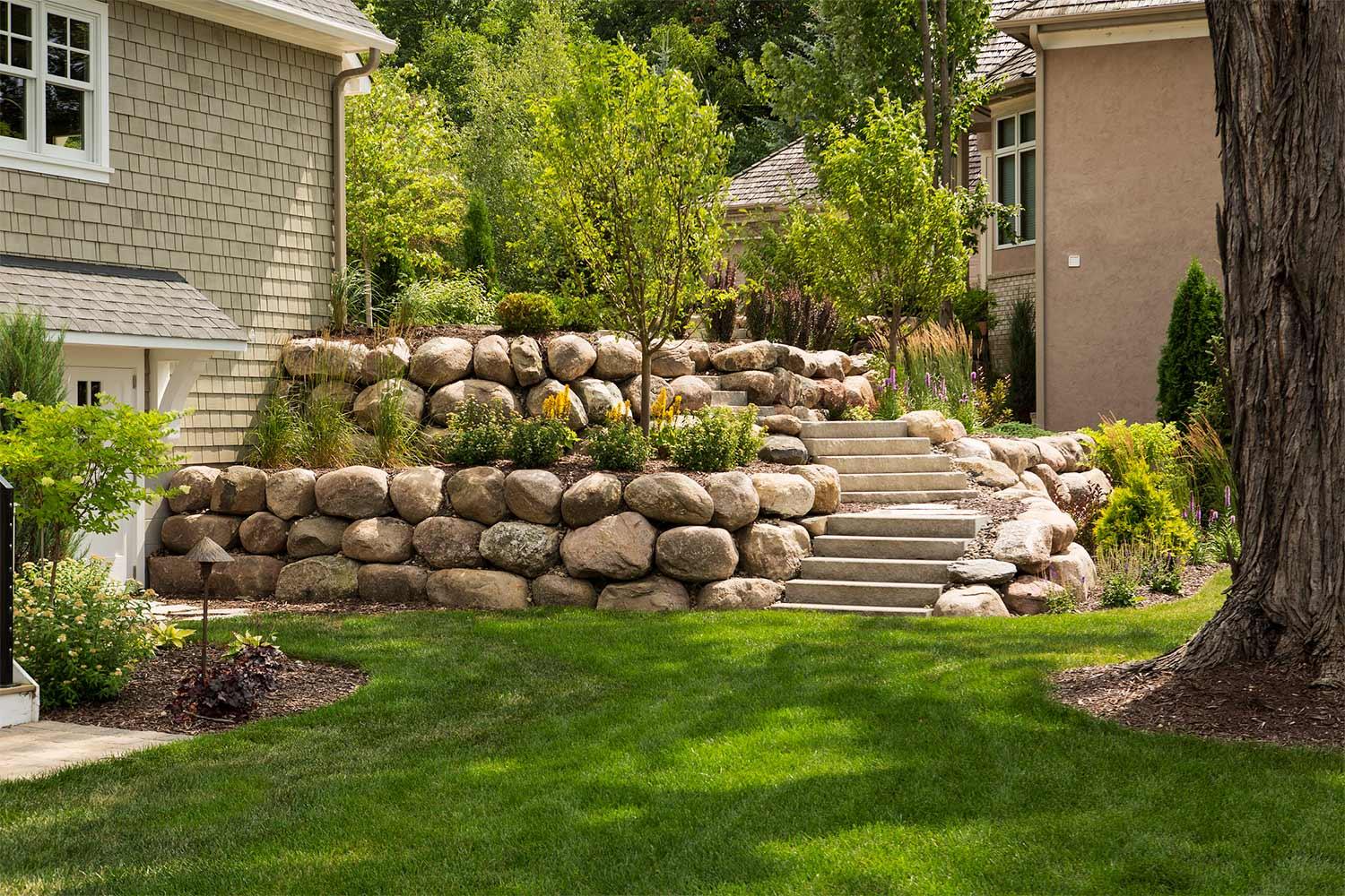 Bright green lawn in the shade. Boulder retaining wall and ornamental trees.